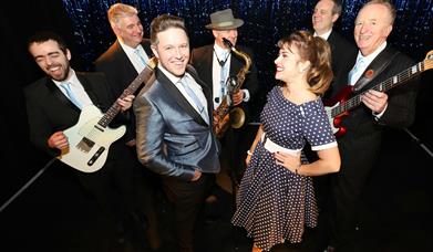 Image shows a band in 50's style dress and musical instruments