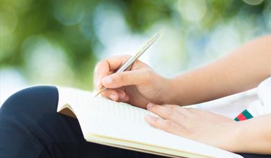 Close up of a person sitting outdoors writing in a note book.