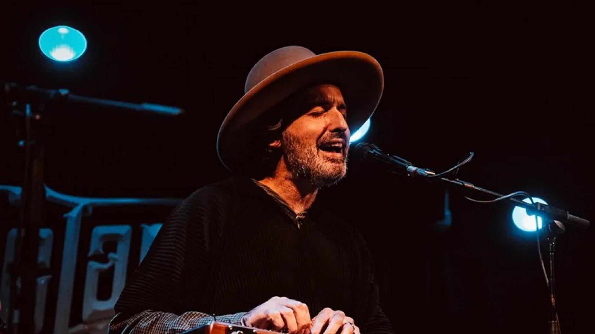 image of musician sitting down singing with eyes closed into microphone.