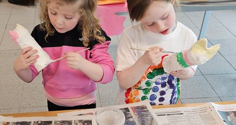 two children are painting papier-mache creations