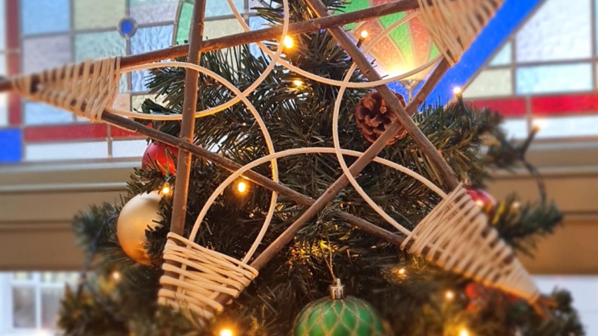 A star made from willow branches sits atop a Christmas tree decorated with lights and baubles. There is a stained glass window in the background. A star made from willow branches sits atop a Christmas tree decorated with lights and baubles. There is a stained glass window in the background.