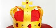 Image of a crown made from yellow and red card.  It has red hearts and jewels attached around the base and there are small gold beads adorning the  bo