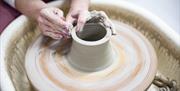 Zara's hand mould the clay while it spins on a potter's wheel