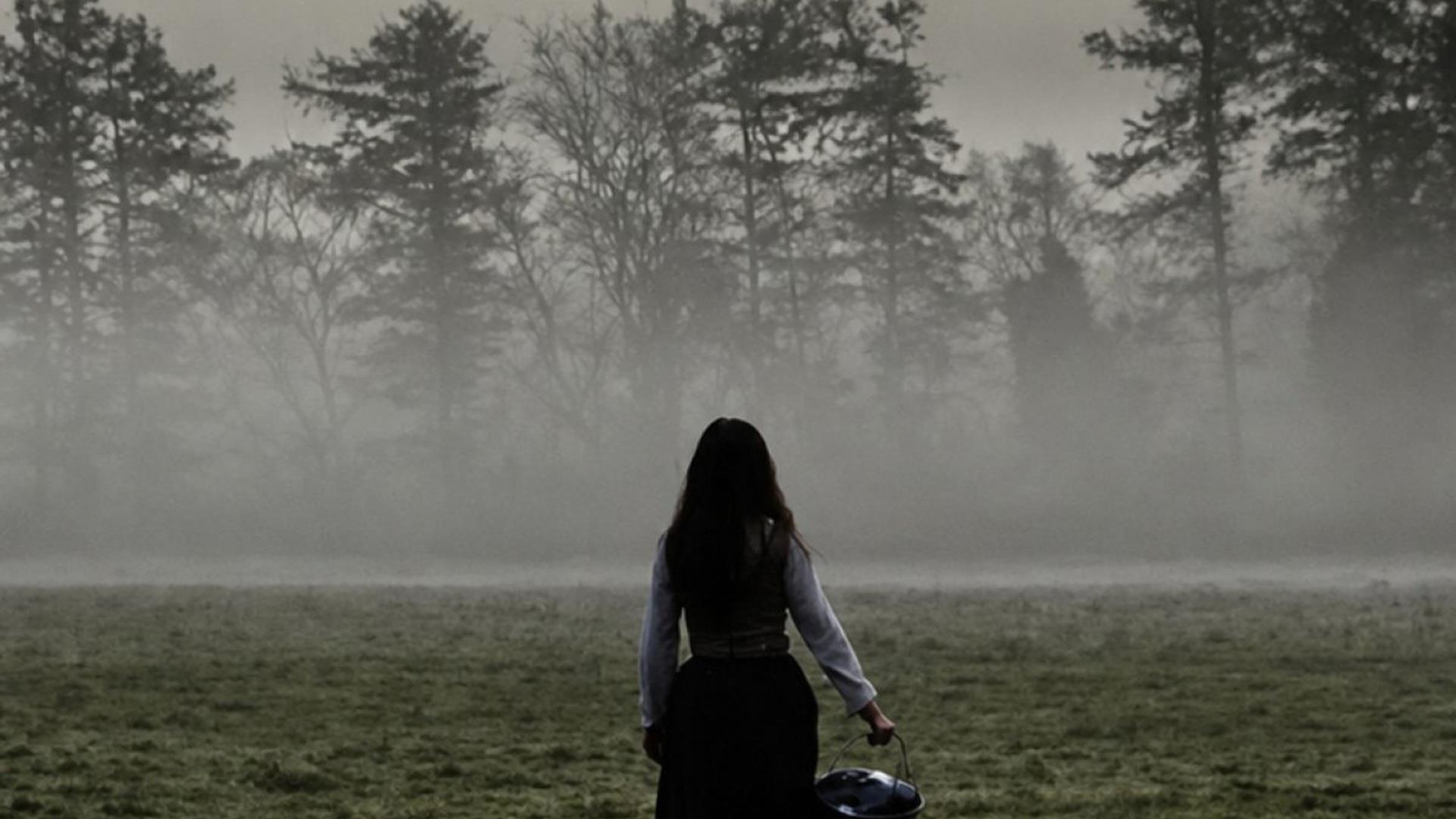 Image showing a girl holding a bucket standing with her back to the camera, in a misty field Image showing a girl holding a bucket standing with her back to the camera, in a misty field
