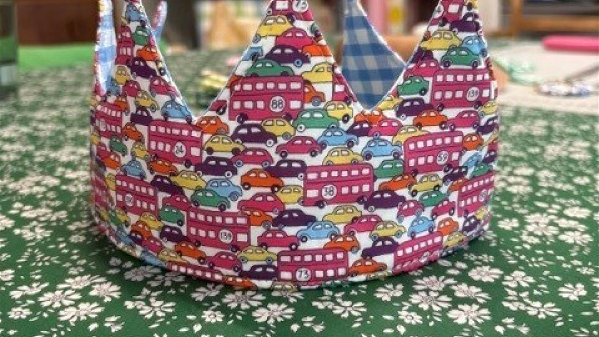 a birthday crown made of printed material that depicts cars and buses sits on a table covered with a green floral tablecloth a birthday crown made of printed material that depicts cars and buses sits on a table covered with a green floral tablecloth