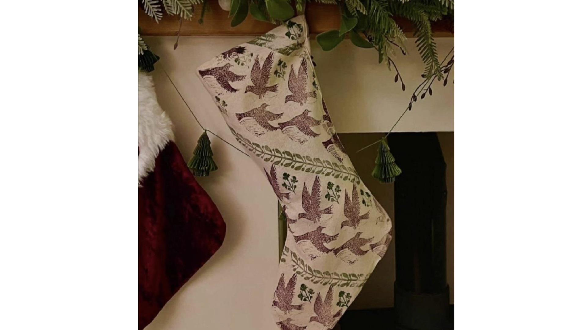 a linen christmas stocking which has been designed with ink printing hangs from a mantlepiece draped with a festive garland a linen christmas stocking which has been designed with ink printing hangs from a mantlepiece draped with a festive garland