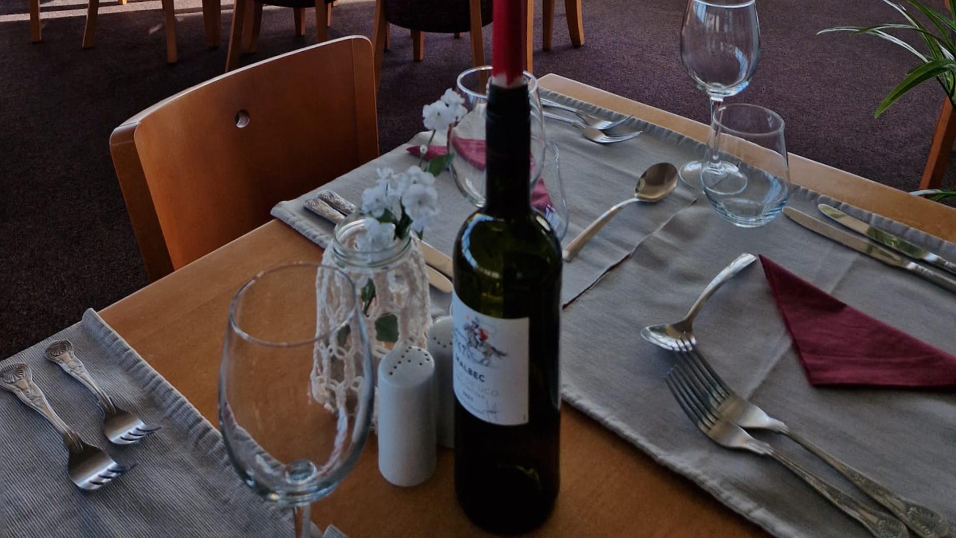 a dinner table set with glasses and cutlery, with a bottle of wine holding a red candle
