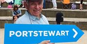 Hugo Duncan holding a blue directional sign that says 'Portstewart' in white writing