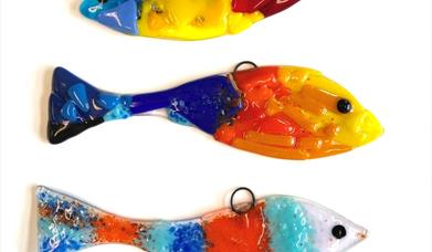 Image shows three brightly coloured fish made from fused glass, one on top of the other