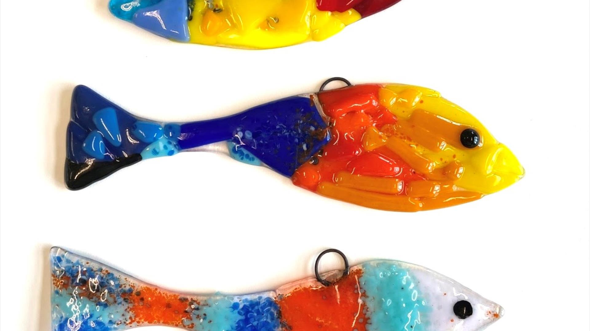 Image shows three brightly coloured fish made from fused glass, one on top of the other