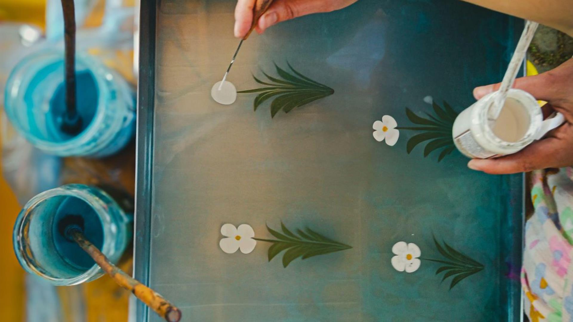 peoples' hands hold a paint brush to paint flowers on a painted flower stalk peoples' hands hold a paint brush to paint flowers on a painted flower stalk