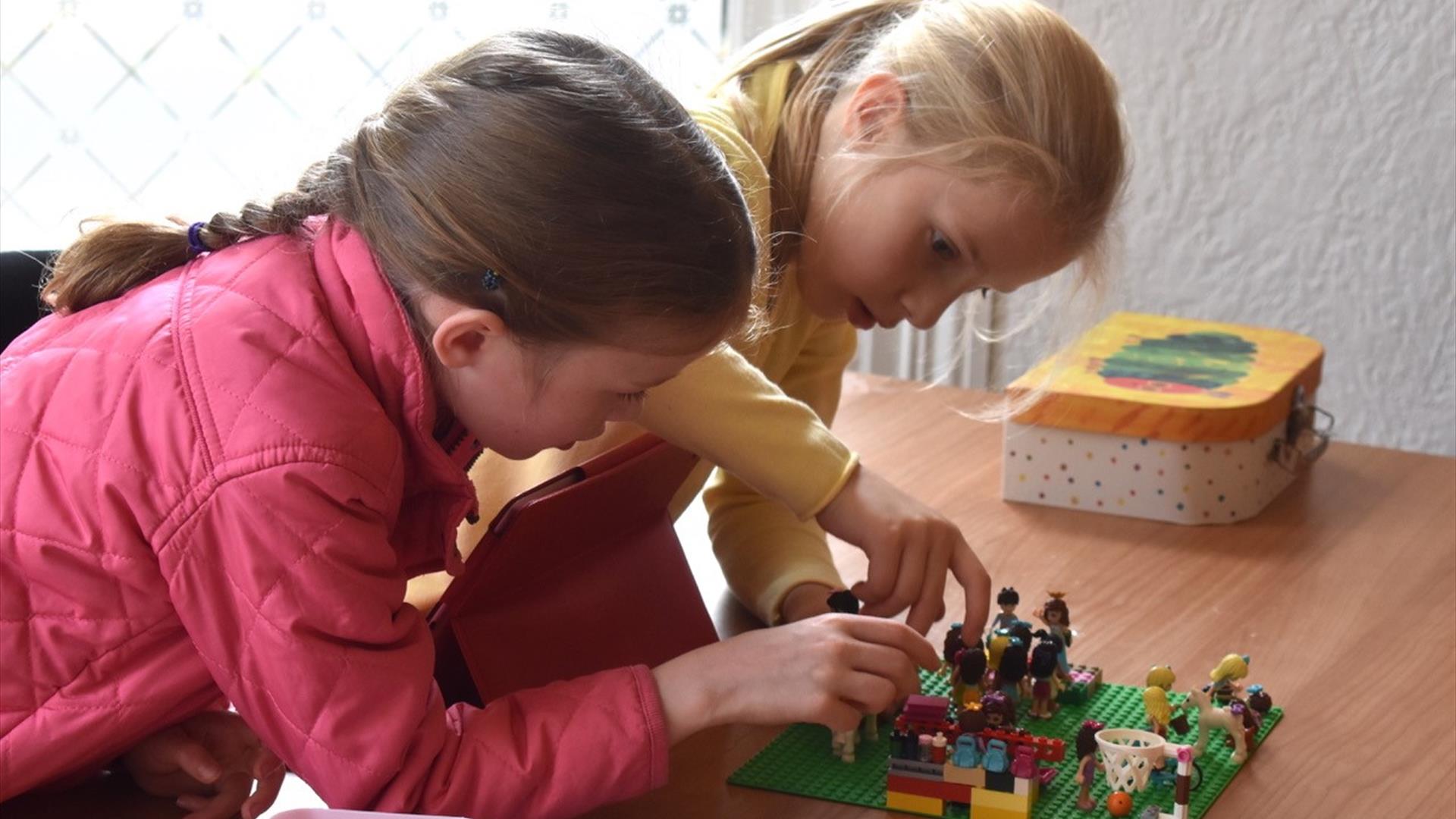 Image shows two young girls building a scene from Lego
