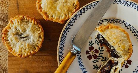 A mince pie cut open with a knife on a plate with two mince pies on the side