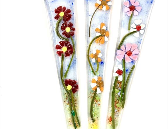 Image shows three glass stakes with flowers in bright colours