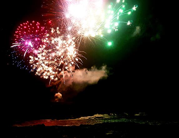Image showing firework exploding in the sky and reflected in the sea below.  The firework is red, green and pink in colour.