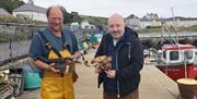 two men holding freshly caught lobster and crab at a harbour