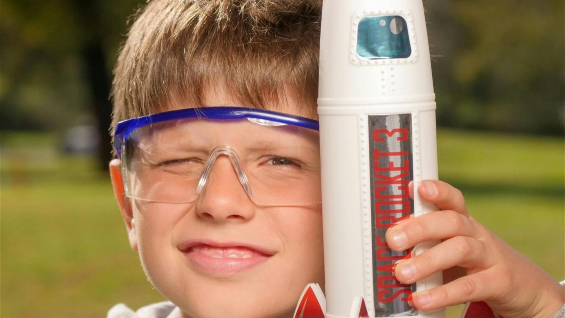 a young boy wearing goggles, holding a model rocket ship a young boy wearing goggles, holding a model rocket ship