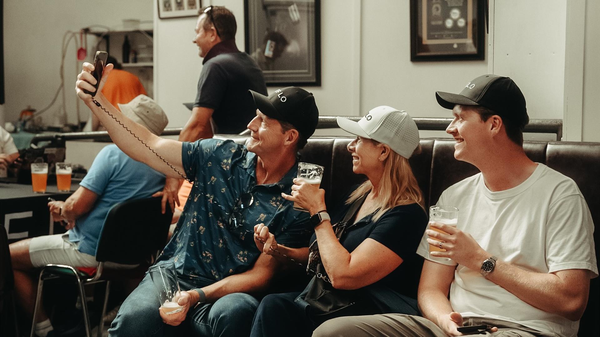 a group of people take a selfie while sitting in a communal area at Lacada Brewery. They are holding beer glasses. a group of people take a selfie while sitting in a communal area at Lacada Brewery. They are holding beer glasses.