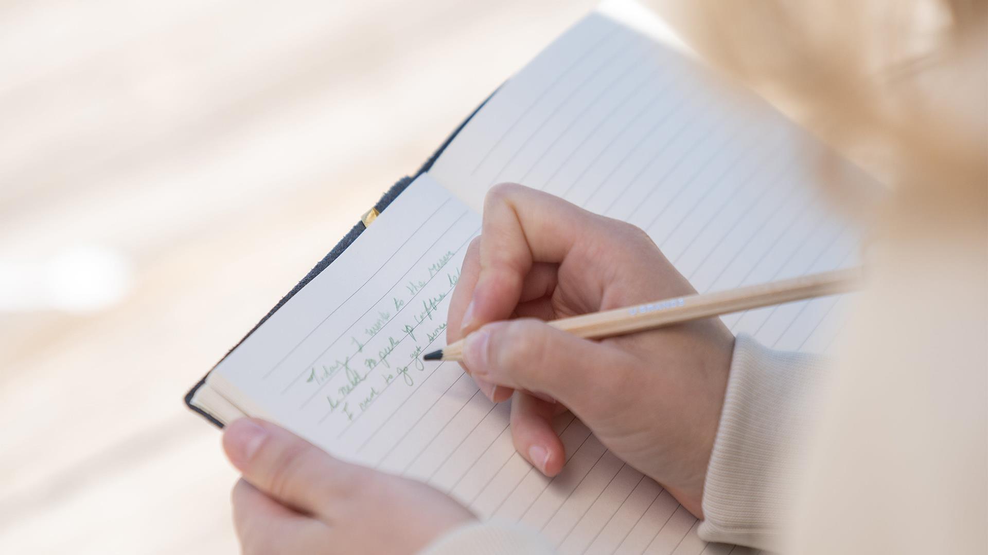 a person's hand writing in a journal with a pencil