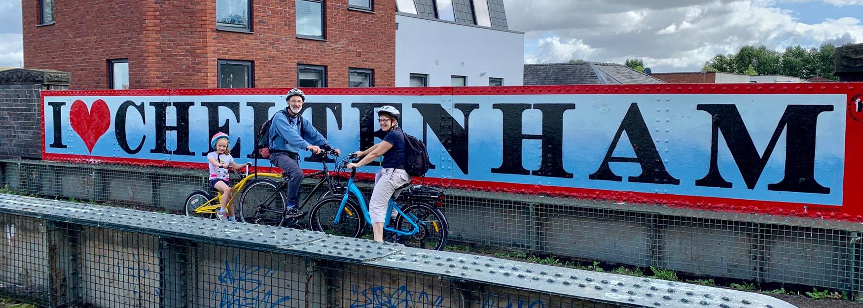 Family on bikes in front of I love Cheltenham street art
