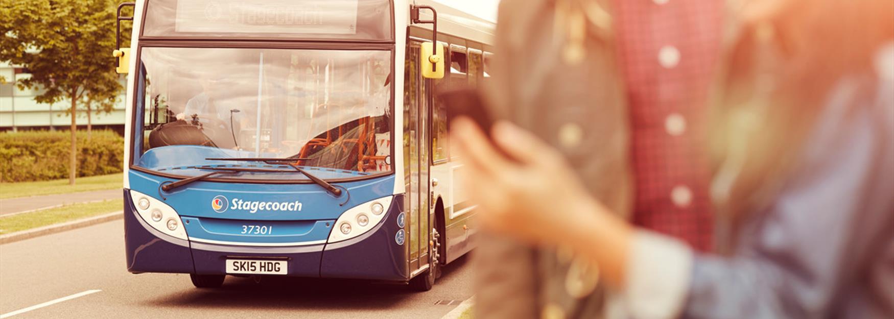 Couple looking at mobile phone at a bus stop, with bus approaching