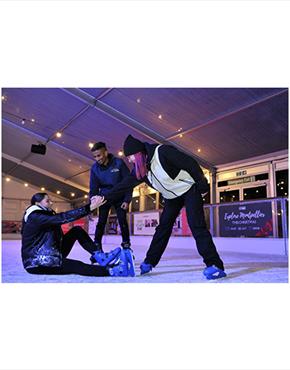 A person being helped up off the floor at an ice rink