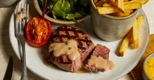 A seared steak with peppercorn sauce accompanied with grilled tomato, chips and green leaves