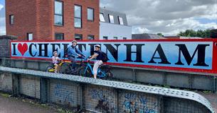 Cyclists in front of a Cheltenham sign