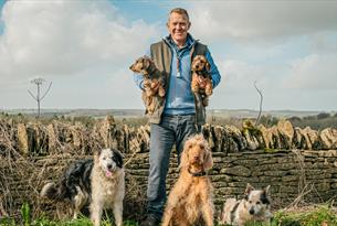 Adam Henson holding 2 dogs, surrounded by dogs