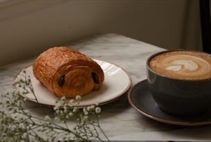 Cup of coffee in a large mug on a marble table top next to a pain au chocolat