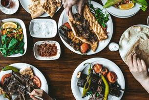 Plates of colourful middle-eastern vegetable and meat dishes set out on a wooden table with salads and dips