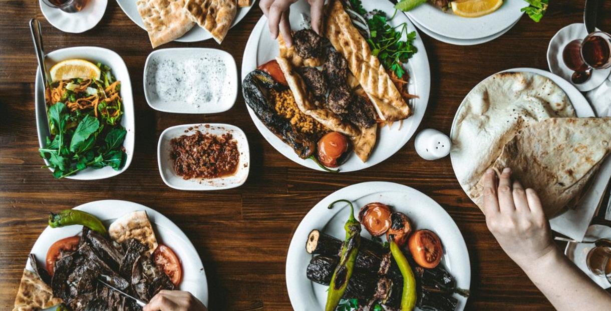Plates of colourful middle-eastern vegetable and meat dishes set out on a wooden table with salads and dips
