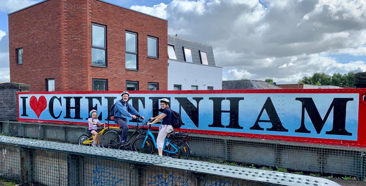 Cyclists in front of a Cheltenham sign