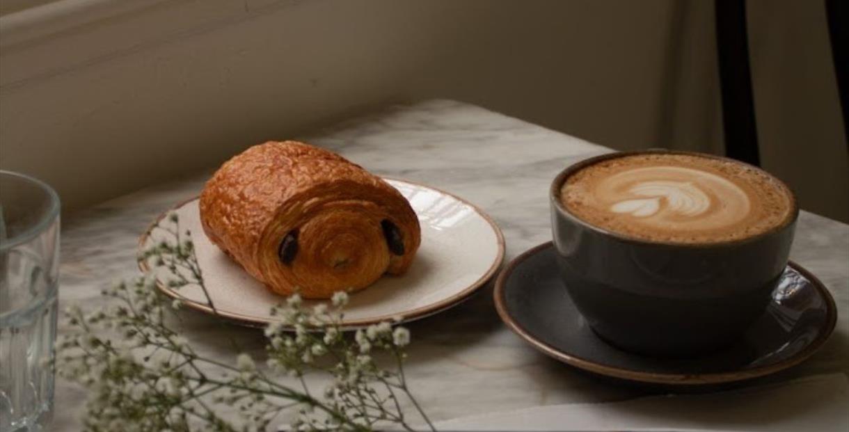 Cup of coffee in a large mug on a marble table top next to a pain au chocolat