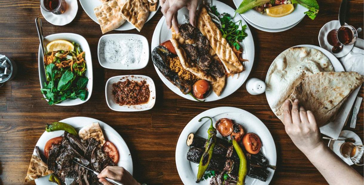 Plates of colourful middle-eastern vegetable and meat dishes set out on a wooden table with salads and dips