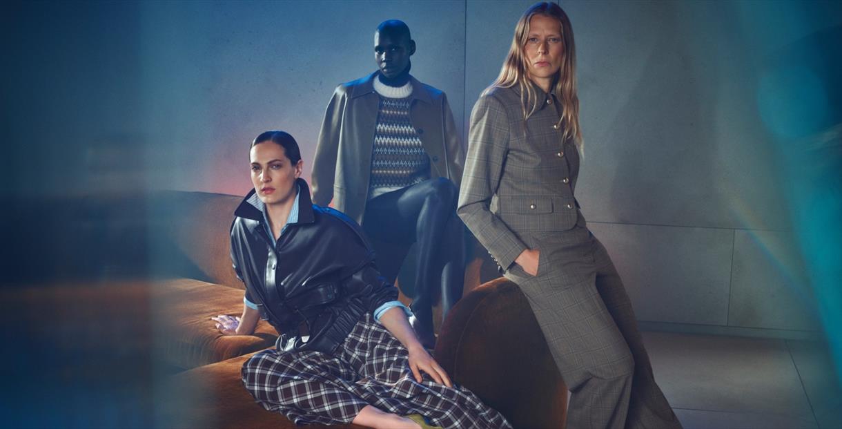 3 adults modelling new Autumn Winter clothes sat on a sofa.