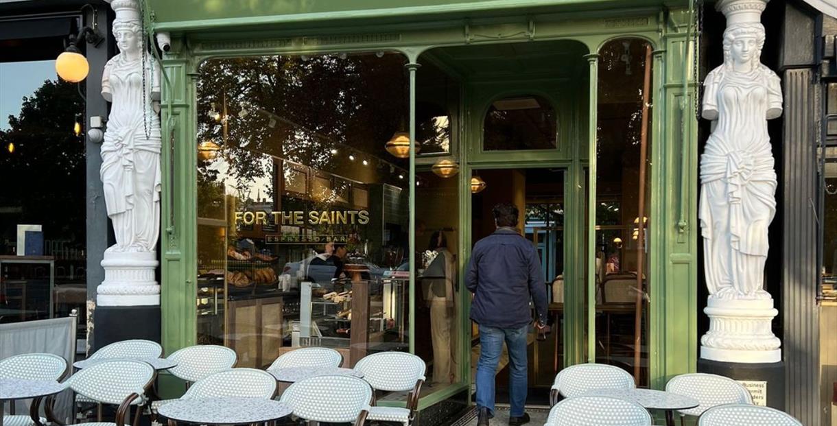 Glass and green painted front of For the Saints espress bar, which stands between two of Montpellier Walk's famous Caryatid statues