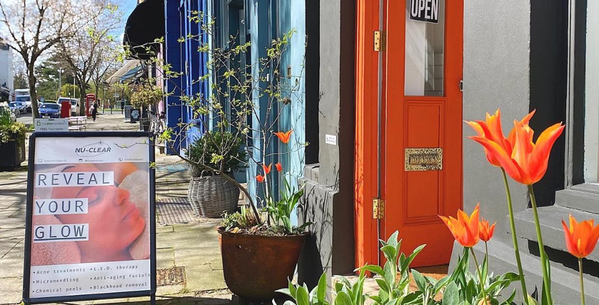 Bright orange tulips in-front of the orange painted door of Nu-Clear facial studio. A-board out front says "Reveal your glow"