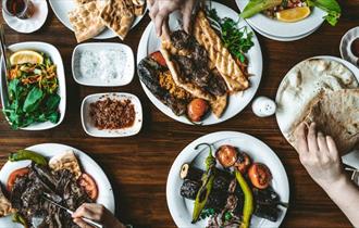 Plates of colourful middle-eastern vegetable and meat dishes set out on a wooden table with salads and dips