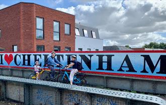 Cyclists in front of a Cheltenham sign