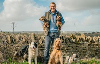 Adam Henson holding 2 dogs, surrounded by dogs