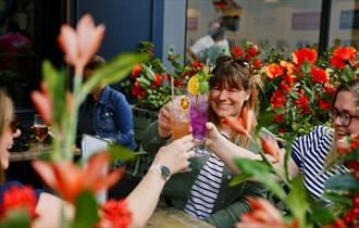 A group of women raising a toast with colourful cocktails in Flight Club's flowery summer terrace