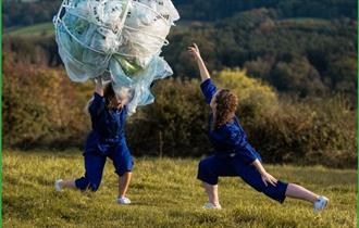 2 performers outside in a field combating plastic waste