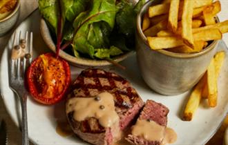 A seared steak with peppercorn sauce accompanied with grilled tomato, chips and green leaves