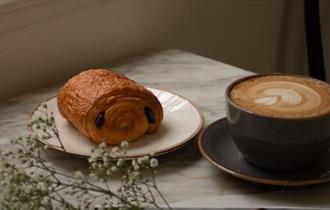 Cup of coffee in a large mug on a marble table top next to a pain au chocolat