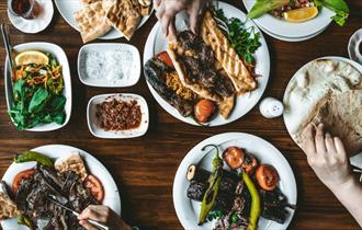 Plates of colourful middle-eastern vegetable and meat dishes set out on a wooden table with salads and dips