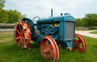 A blue vintage Fordson tractor with faded red wheels sits on a grassy patch at Cotswold Farm Park