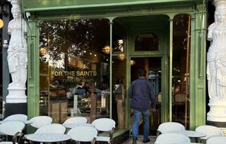 Glass and green painted front of For the Saints espress bar, which stands between two of Montpellier Walk's famous Caryatid statues