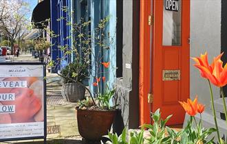 Bright orange tulips in-front of the orange painted door of Nu-Clear facial studio. A-board out front says "Reveal your glow"