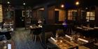 Wooden tables set with cutlery, napkins and wine glasses in a dark-painted and wood-panelled restaurant with soft lighting